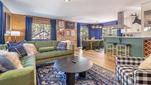 Ein gemütliches Wohnzimmer mit einem grünen Sofa, einem runden Couchtisch und einem Essbereich mit Holztisch und Stühlen.