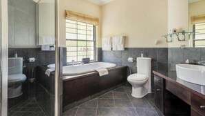 Ein modernes Badezimmer mit Badewanne, Toilette und Waschbecken, ausgestattet mit dunklen Fliesen und einem großen Spiegel.