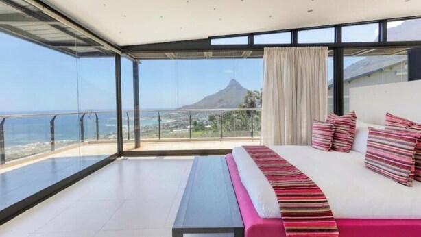 Ein modernes Hotelzimmer mit einem großen Bett, einer Bank und einem Balkon mit Blick auf einen Berg und das Meer.