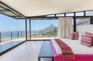 Ein modernes Hotelzimmer mit einem großen Bett, einer Bank und einem Balkon mit Blick auf einen Berg und das Meer.