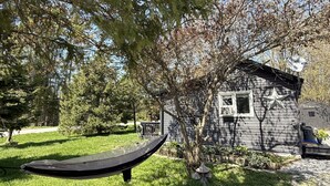 Una cadira d'hamaca sota un arbre, una casa petita amb una decoració d'estrella i un cel serè.