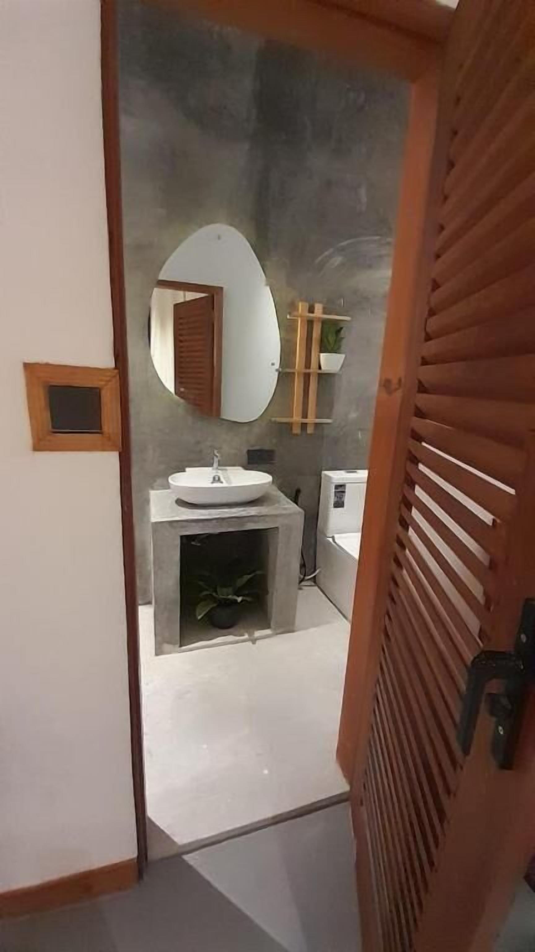 Un baño moderno con un espejo redondo, un lavabo y una planta pequeña.