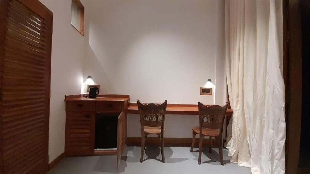 A small room with a desk, two chairs, a lamp, and a window with curtains.