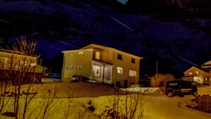 A mountain landscape at night with a house in the foreground and the aurora borealis in the sky.