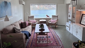 A cozy living room with a sofa, chairs, a coffee table, and a view of the sea.