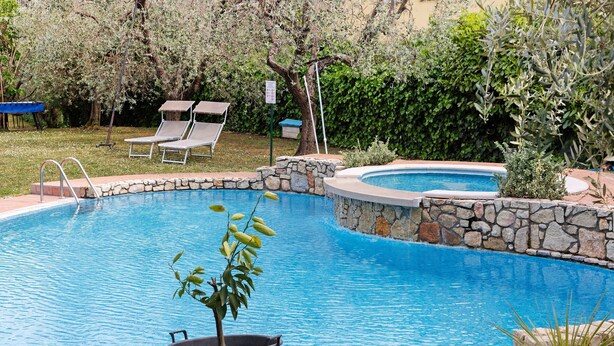 Piscina com borda de pedra, cadeiras de descanso e um vaso com planta.