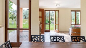 Uma sala de jantar com mesa e cadeiras, um barril de madeira e vista para um jardim através de portas de vidro.