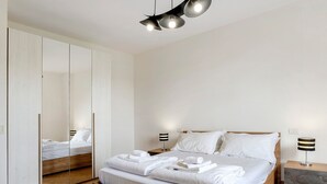 Quarto moderno com cama, mesas de cabeceira, espelho e luminária no teto.