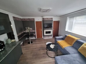 Ein gemütlicher Wohnbereich mit Küchenzeile, einer Couch mit gelbem Kissen, einem kleinen runden Tisch und einem Kamin.