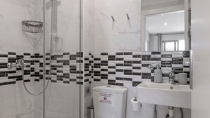 Un bagno moderno con cabina doccia in vetro, un water bianco, un lavandino con specchio e un cestino.