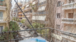 Un balcone con tavolo e sedie, avvolto da edera e affacciato su un quartiere residenziale.