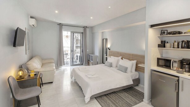 Una moderna camera d'albergo con un letto, un'area salotto con una poltrona, un angolo cottura e un balcone con vista.