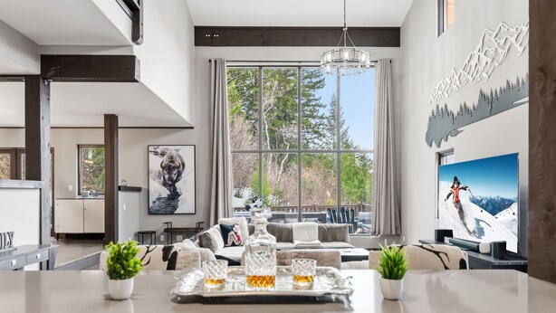 Eine moderne Küche mit einer großen Kochinsel, einem Essbereich mit einer Couch und Blick auf Bäume durch große Fenster.
