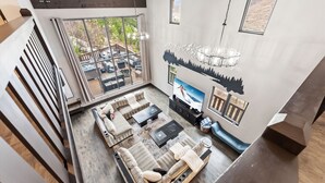 Ein modernes Wohnzimmer mit einem Ecksofa, einem Flachbildfernseher und einem großen Fenster mit Blick auf eine Terrasse.