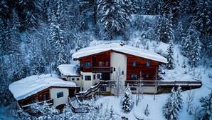 Eine schneebedeckte Lodge mit einem zweistöckigen Hauptgebäude, einem kleineren Anbau und einer verschneiten Terrasse.