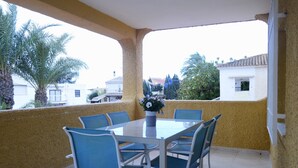 Un espace extérieur abrité, aménagé pour les repas, avec une table et des chaises, un pot de fleurs et une vue sur les bâtiments environnants.