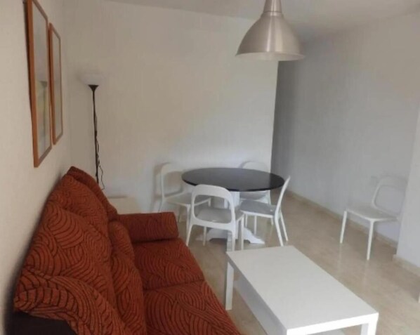 Un soggiorno con divano, tavolo da pranzo con sedie, lampadario a sospensione e lampada da terra.