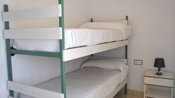 Una cama litera de dos plazas, una mesita de noche con lámpara y un enchufe en la pared.