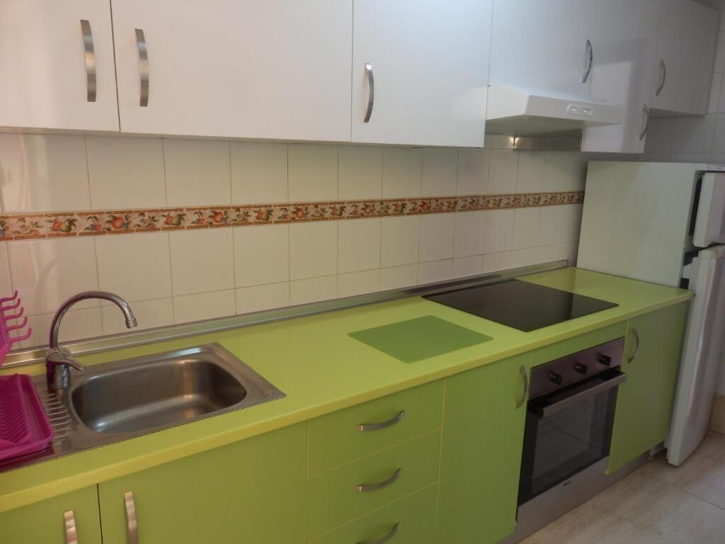 Eine Küche mit weißen Schränken, einer grünen Arbeitsplatte, einem Edelstahlspülbecken und einem eingebauten Backofen.