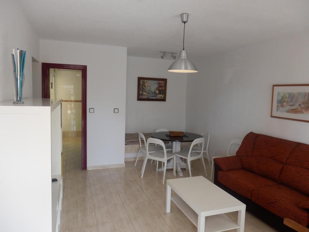 A compact living space with a dining area, a sofa, a pendant light, and a door leading to another room.