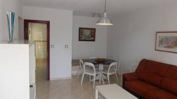 A compact living space with a dining area, a sofa, a pendant light, and a door leading to another room.