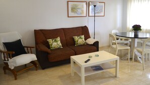 Un salon avec un canapé marron, une table basse blanche, un fauteuil en bois et une table à manger avec des chaises.