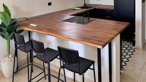 A modern kitchen with a wooden island, black bar stools, a potted plant, and a black door. - ALSAWAH Modern 2BR Apartment - Madinty (Second New cairo)