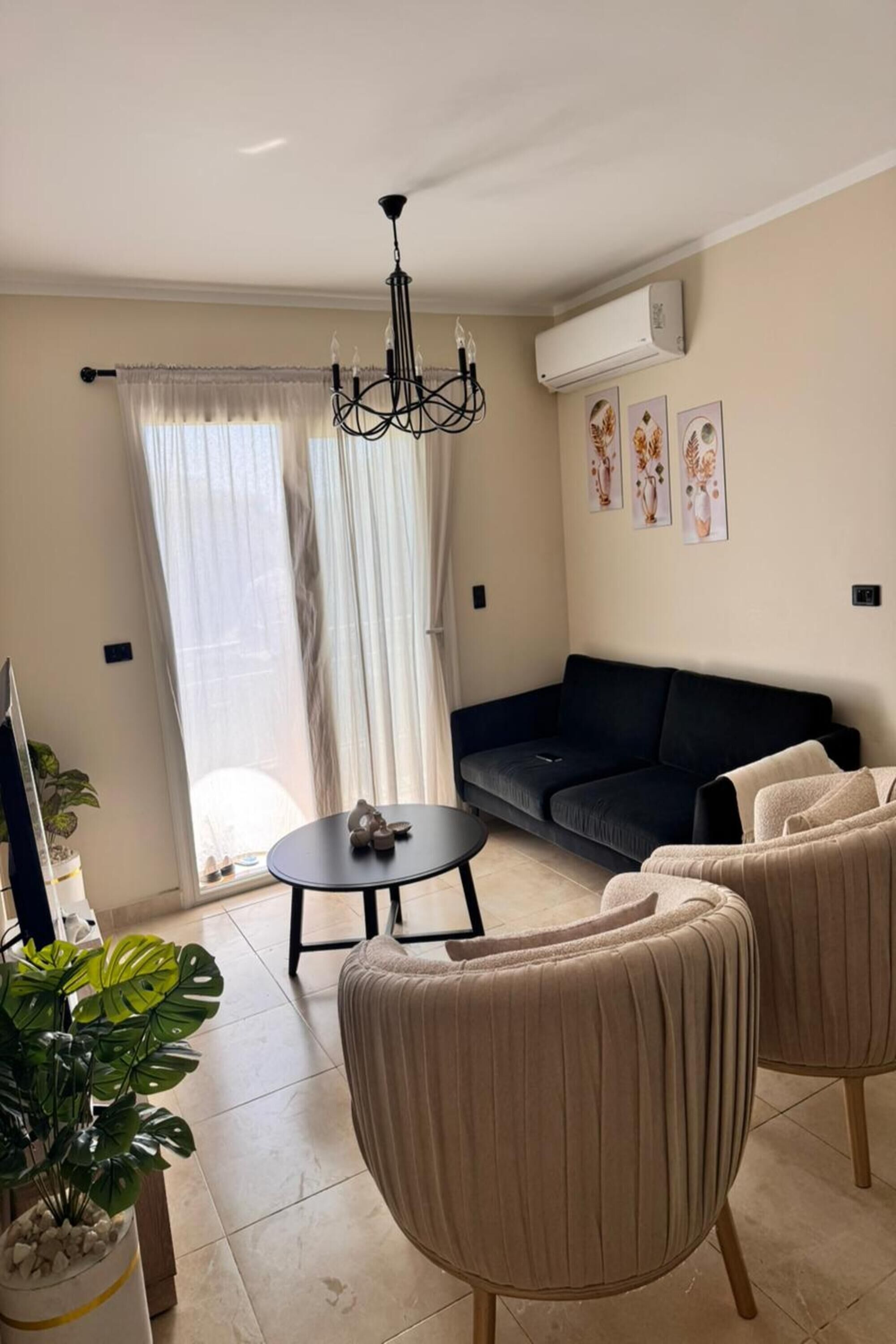 A living room with a sofa, two armchairs, a small table, a chandelier, and a potted plant.