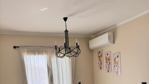 A living room with a sofa, two armchairs, a small table, a chandelier, and a potted plant. - ALSAWAH Modern 2BR Apartment - Madinty (Second New cairo)