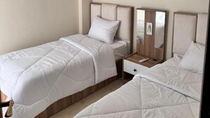 A hotel room with two single beds, a bedside table with a mirror, a wall-mounted artwork, and a hanging light fixture. - ALSAWAH Modern 2BR Apartment - Madinty (Second New cairo)