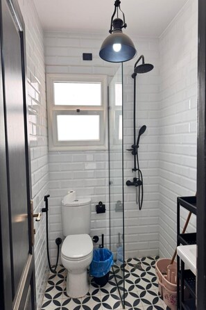 Ein Badezimmer mit Toilette, Dusche, Fenster und einem Musterfußboden.