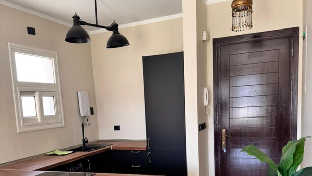 A kitchen with a wooden countertop, black chairs, a dark door, and a hanging light fixture. - ALSAWAH Modern 2BR Apartment - Madinty (Second New cairo)
