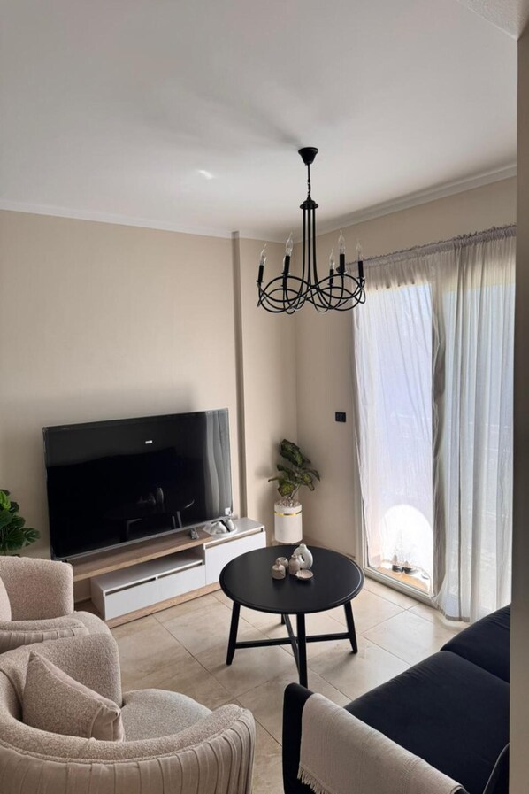 Ein Wohnzimmer mit Flachbildfernseher, einem schwarzen Couchtisch, einer Couch und einer Kristallleuchtre.'