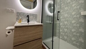 Ein modernes Badezimmer mit Duschkabine aus Glas, einem runden Spiegel und einem Holzwaschtisch.