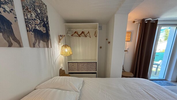 Ein Schlafzimmer mit einem Bett, einer Hängelampe, einem Kleiderschrank und Blick durch eine Tür.