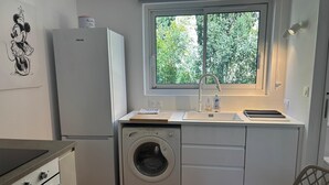 Eine kompakte Küche mit Waschmaschine, Kühlschrank, einem Fenster mit Blick auf Grünflächen und einem Essbereich mit Tisch und Stuhl.