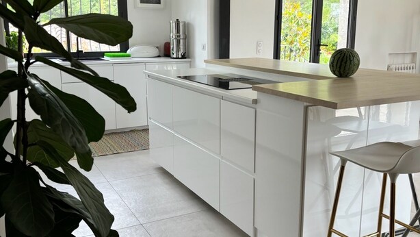 A modern kitchen with white cabinetry, a black pendant light, a large window with a view of greenery, and a plant in the foreground. - Bastide provençale - Private pool 11m - Air conditioning - Pizza oven - Aix 5min (Aix-en-Provence)