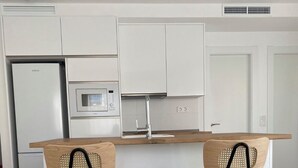 Eine moderne Küche mit weißen Schränken, einer Mikrowelle und einem Spülbecken. Zwei Hocker mit gewobenen Sitzen und schwarzen Metallbeinen sind vorhanden.