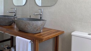 Ein Badezimmer mit zwei steinernen Waschbecken, einem Holzkosmetikschrank, großen Spiegeln und einer weißen Toilette.