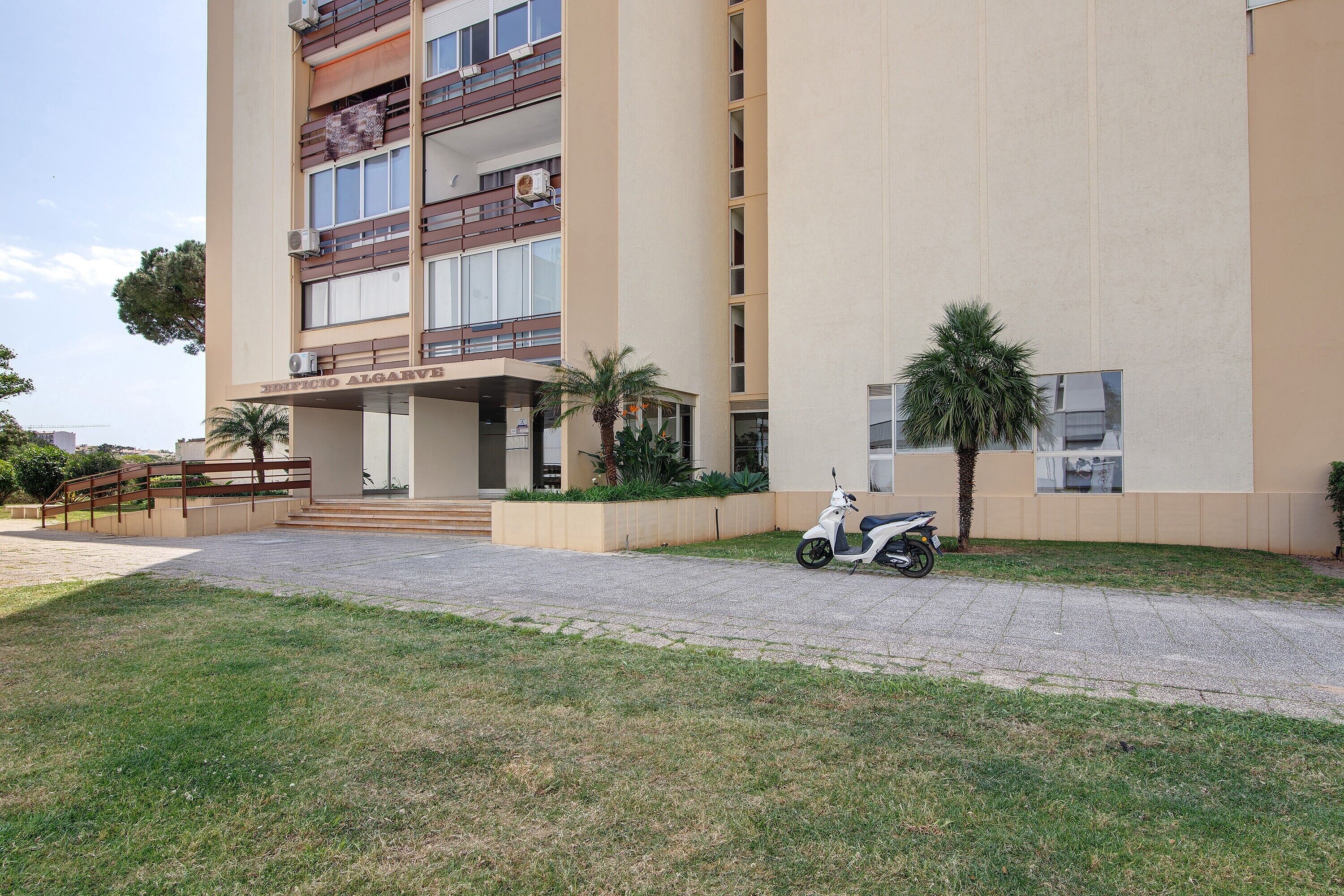 A multi-story building with a flat facade, a paved entrance area, and a parked scooter.