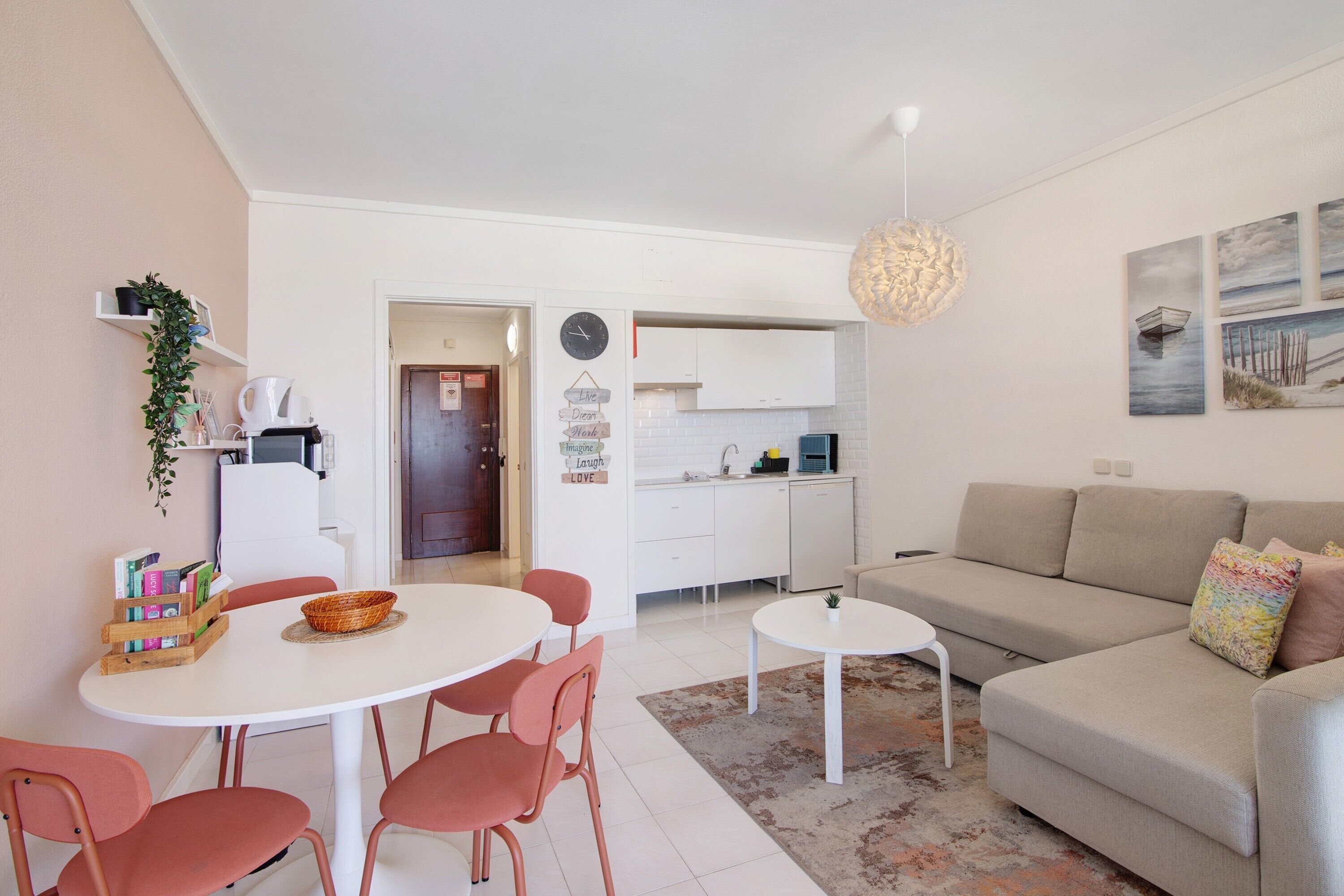 A modern living room with a sofa, a dining table with chairs, a kitchen area, and a hallway.