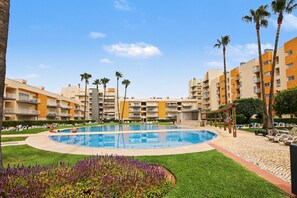 A swimming pool surrounded by palm trees and a building with balconies. - Holiday Home 'Brisa Do Mar Moura Beach' with Shared Pool, Shared Garden and Wi-Fi (Quarteira)