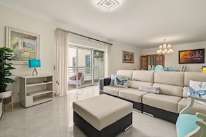A modern living room with a sofa, ottoman, and a TV stand. - Holiday Home 'Brisa Do Mar Moura Beach' with Shared Pool, Shared Garden and Wi-Fi (Quarteira)