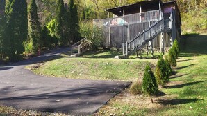 A cabin with a porch and steps, surrounded by trees and a paved driveway. - RiverFront Cabin in New River Gorge National Park & Preserve (Prince)