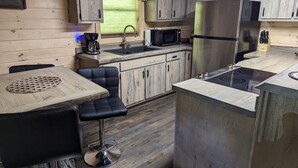 A compact kitchen with a sink, microwave, refrigerator, and a small dining area with a table and chair. - RiverFront Cabin in New River Gorge National Park & Preserve (Prince)