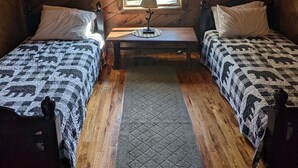 A cabin room with two beds, a small table, a window with curtains, and wooden walls. - RiverFront Cabin in New River Gorge National Park & Preserve (Prince)