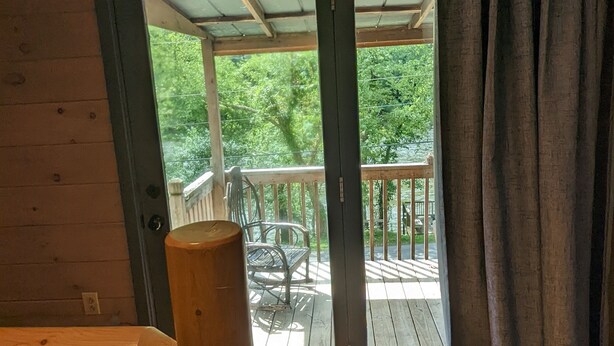 A wooden interior with a sliding glass door leading to an outdoor deck with a table and chairs. - RiverFront Cabin in New River Gorge National Park & Preserve (Prince)
