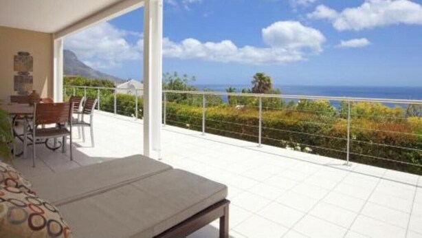 Ein Balkon mit Meerblick, ein Essbereich mit Stühlen und eine Couch.