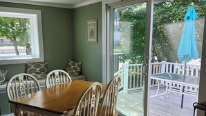 Un comedor con mesa y sillas de madera, ventilador de techo, ventana con vistas al exterior y puerta corrediza de vidrio que da a una terraza.