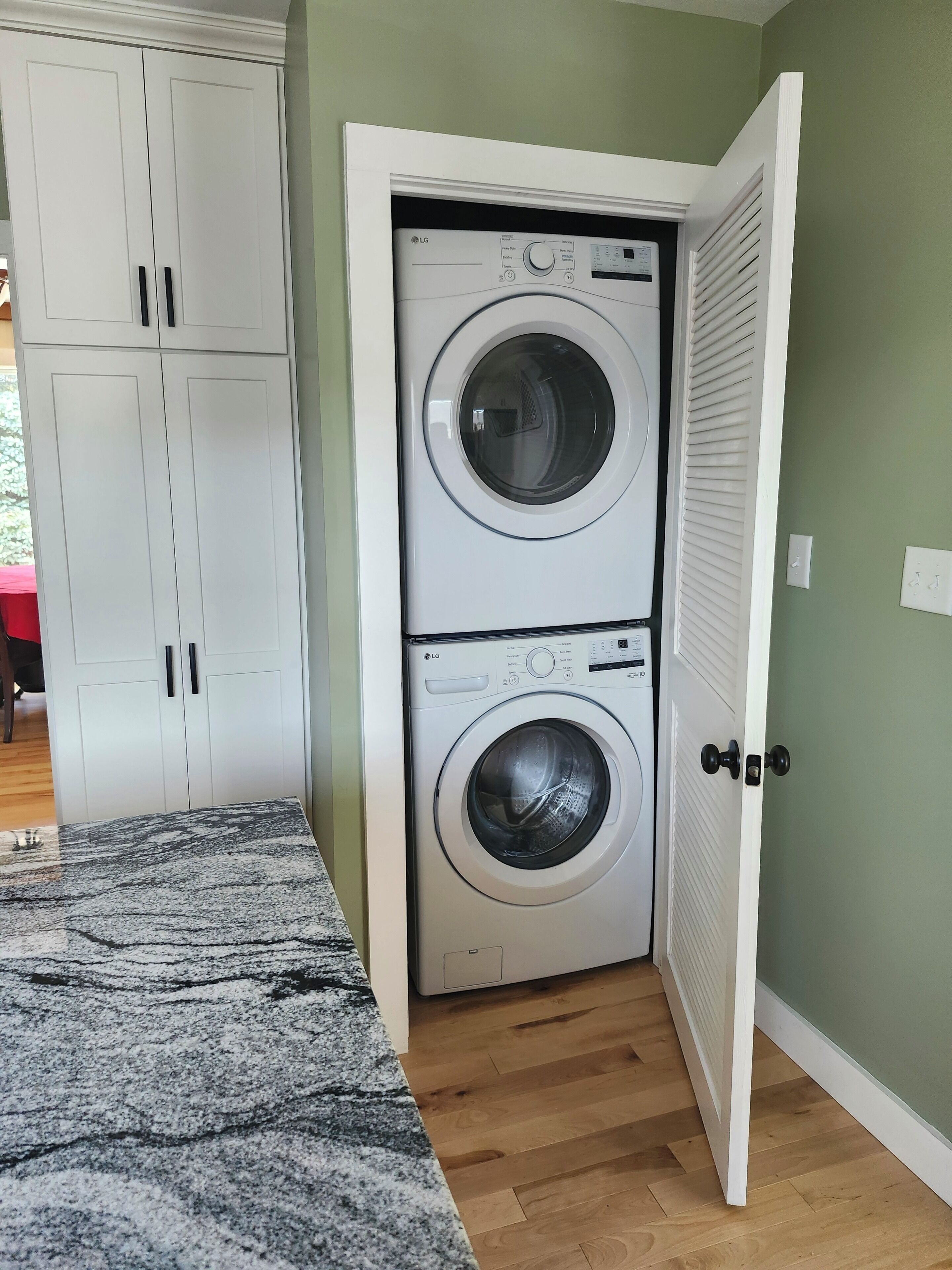 A laundry room with two stacked washing machines, a wooden floor, and a white door.